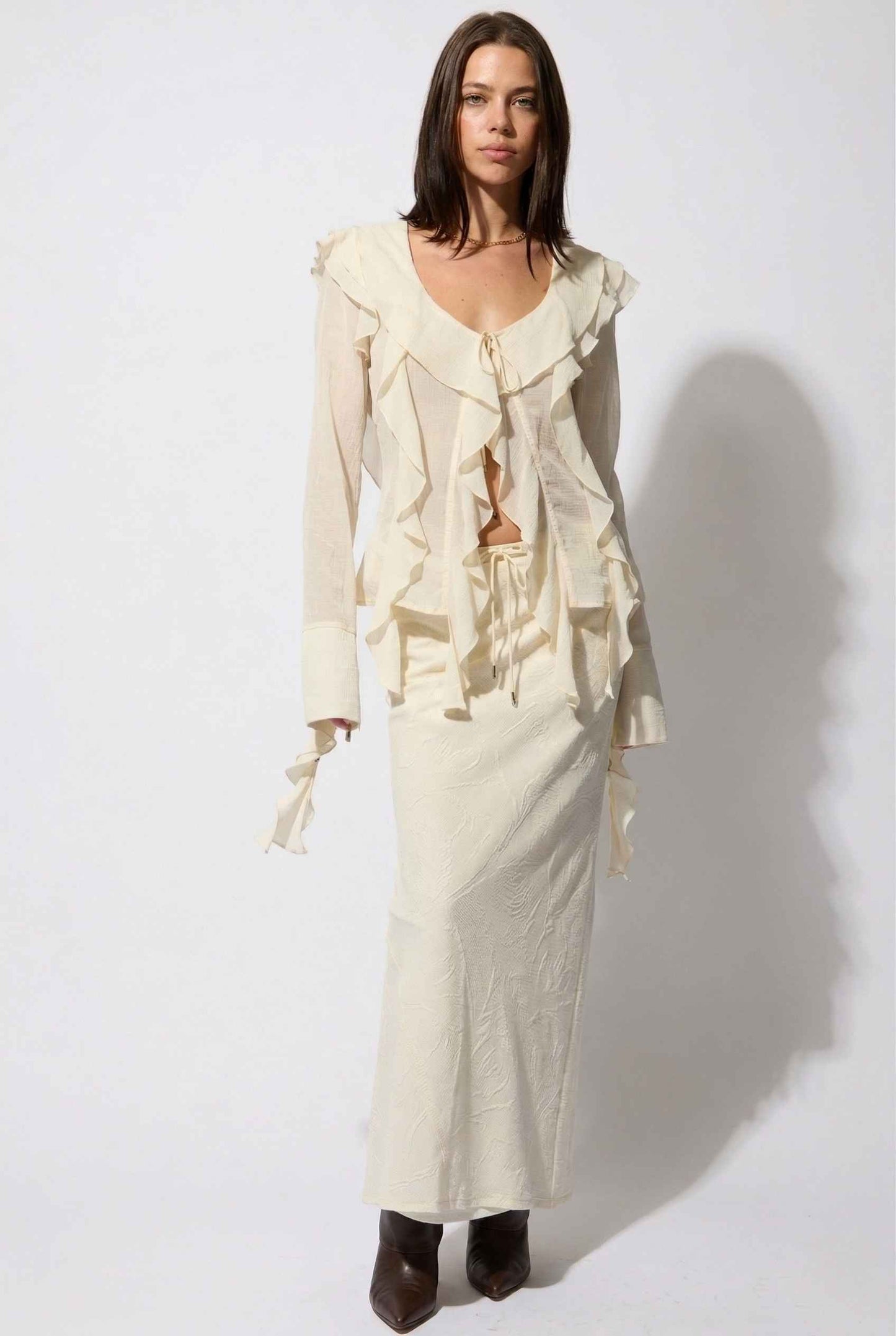 Model wearing Veda Skirt in Cream Satin Drawstring Maxi Skirt paired with matching ruffle tie bouse and booties