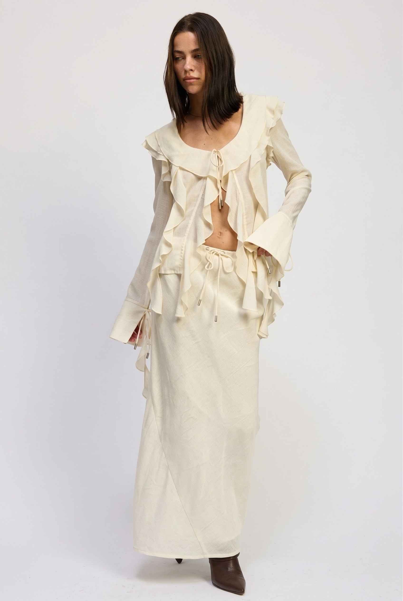 Model wearing Veda Skirt in Cream Satin Drawstring Maxi Skirt paired with matching ruffle tie bouse and booties