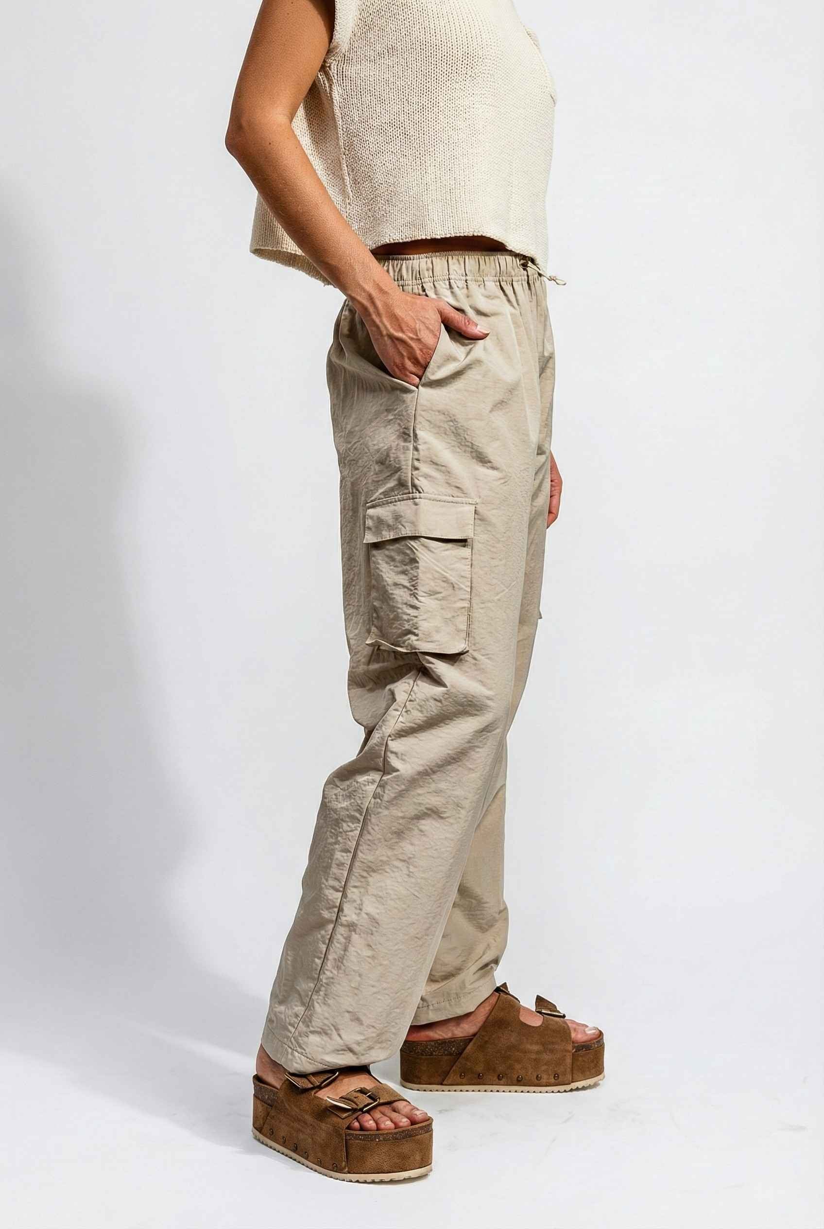 Model wearing Wren Pants 100% Nylon Parachute Cargo Pants in Taupe with t-shirt and platform sandals on plain background