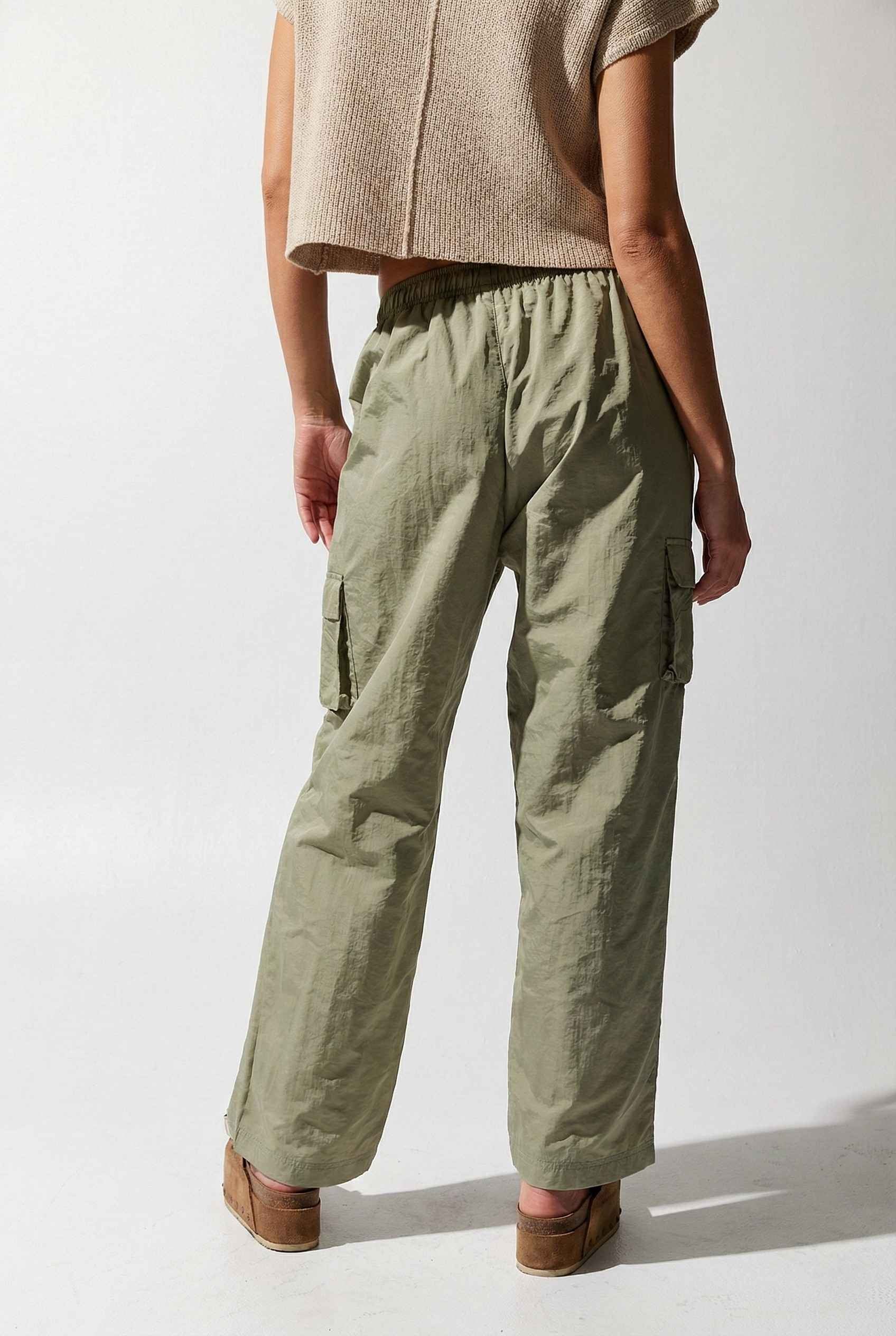 Model wearing Wren Pants 100% Nylon Parachute Cargo Pants in Olive with t-shirt and platform sandals on plain background
