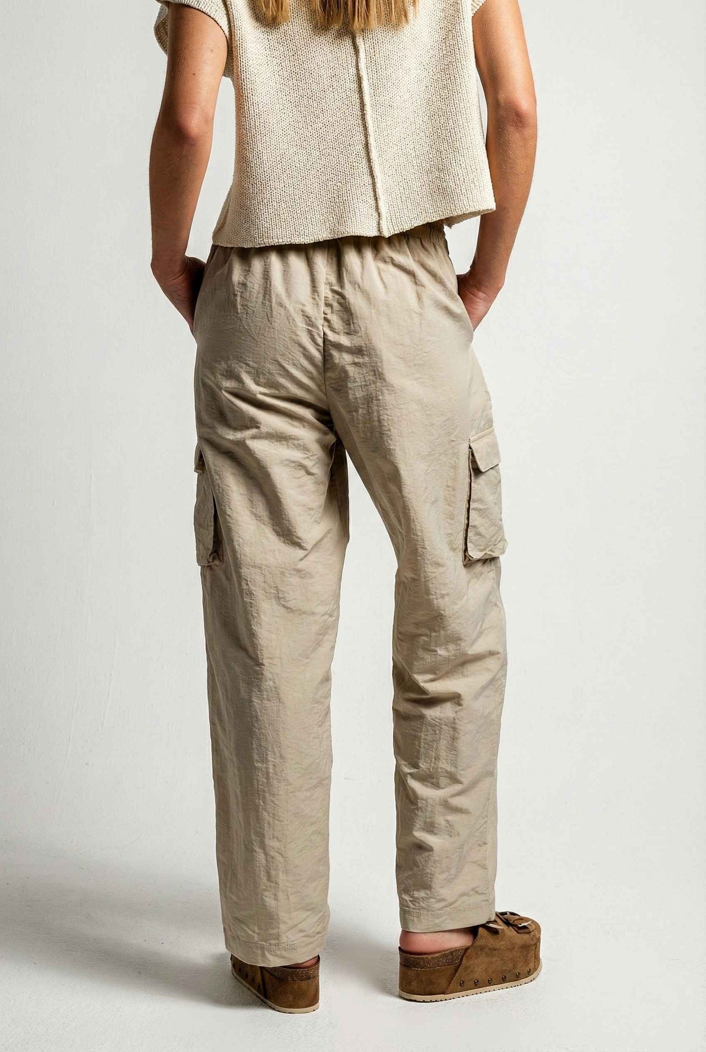 Model wearing Wren Pants 100% Nylon Parachute Cargo Pants in Taupe with t-shirt and platform sandals on plain background