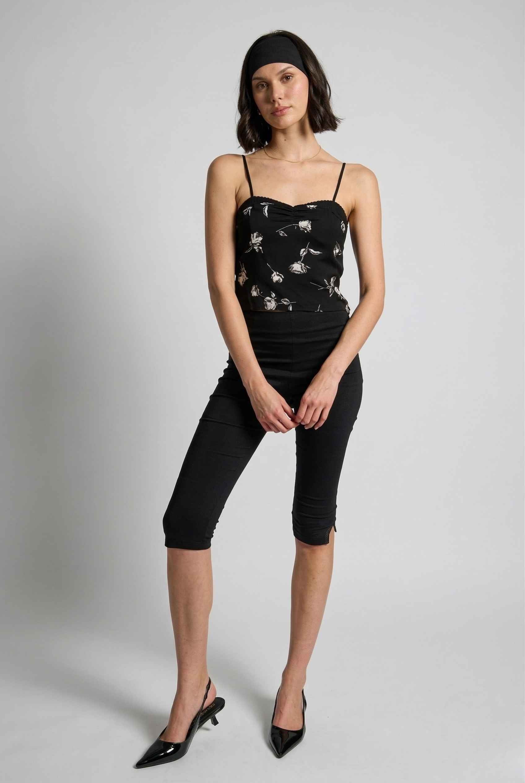 Woman wearing a Zara Top Black & White Rose Print Cotton Lace Trim Camisole with white floral patterns on a gray background