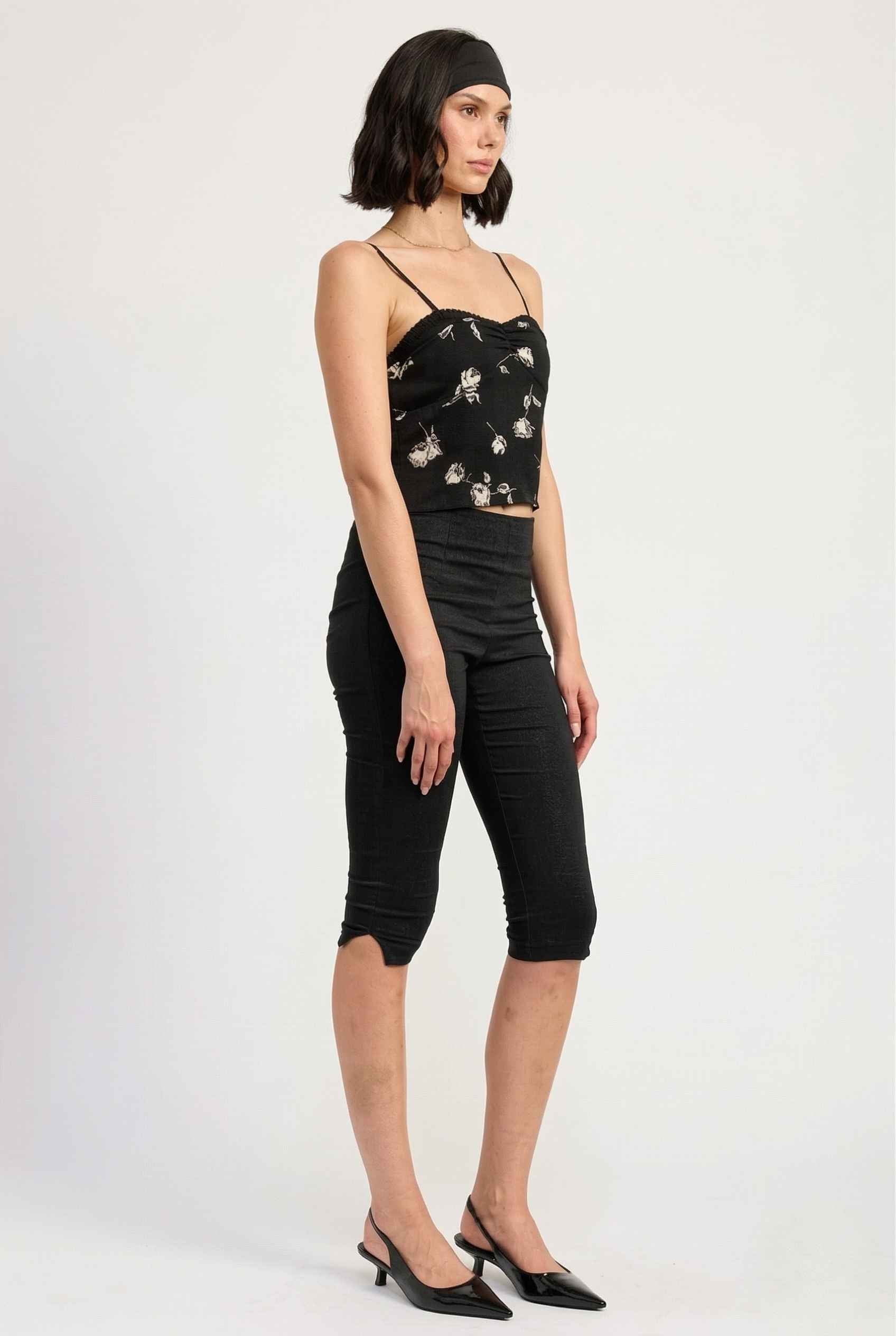 Woman wearing a Zara Top Black & White Rose Print Cotton Lace Trim Camisole and black capri pants on a white background