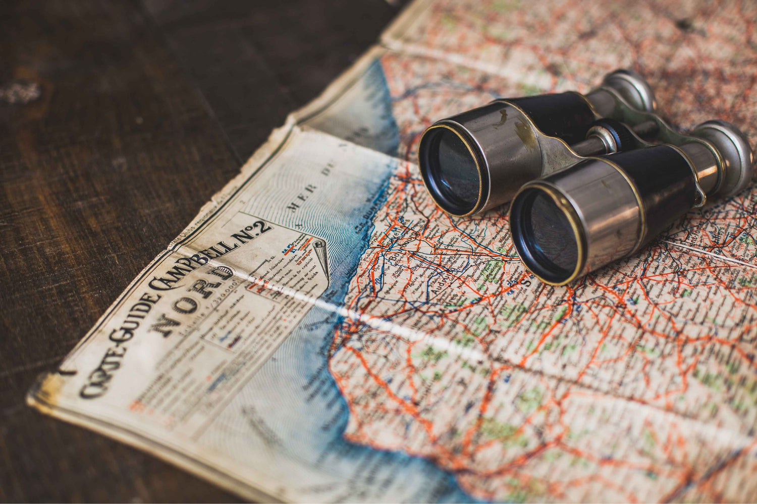 Binoculars on an old map with a paper guidebook