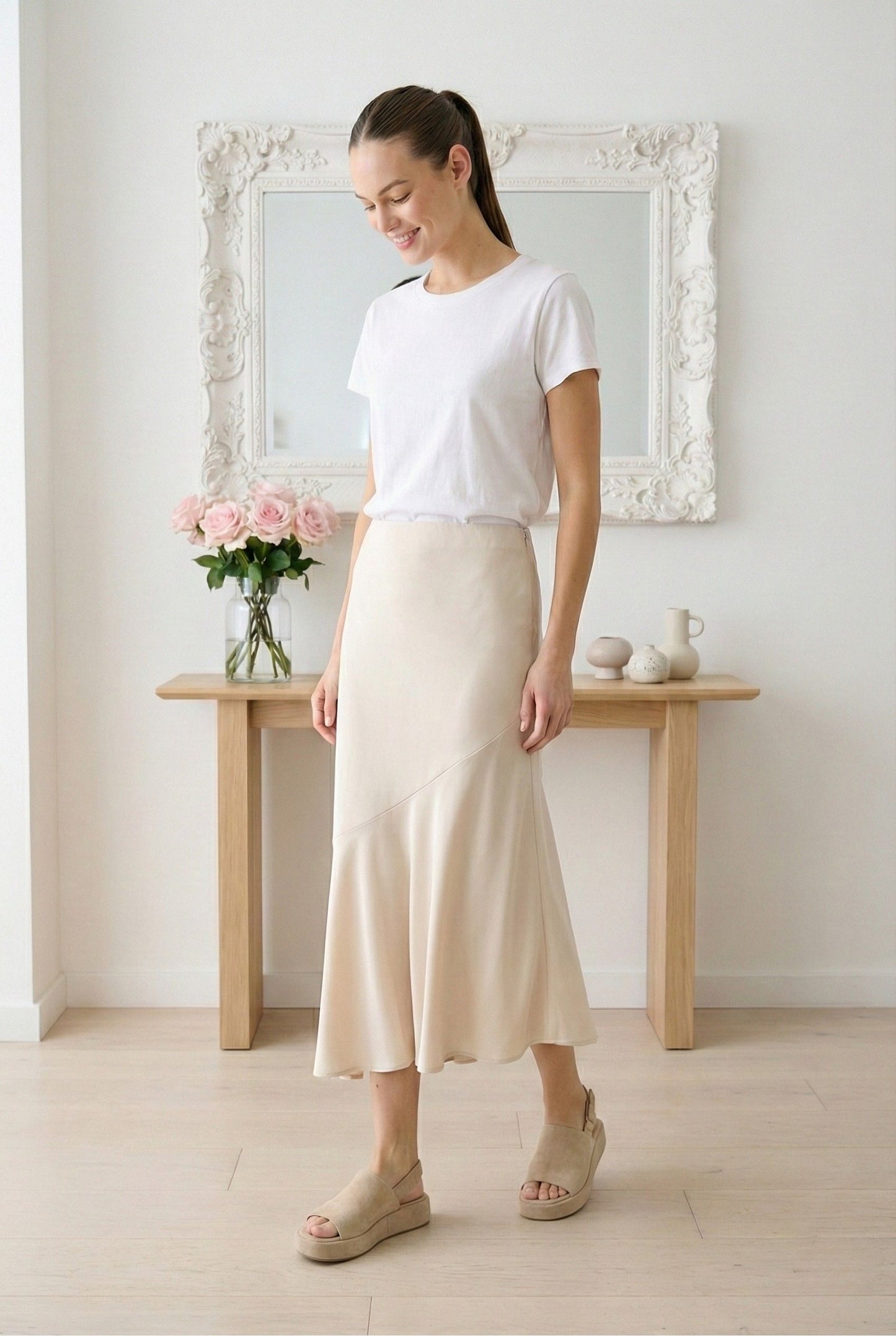Model wearing Emory Park asymmetrical ruffle hem skirt in Taupe worn with tee and espadrille sandals standing in minimalist home with roses
