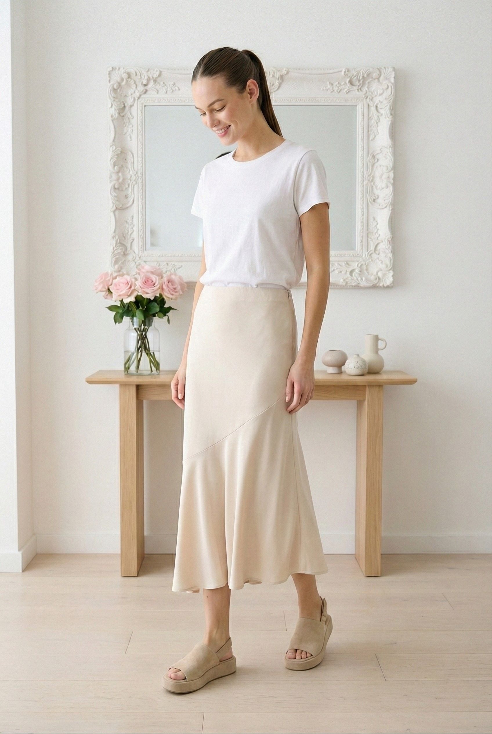 Model wearing Emory Park asymmetrical ruffle hem skirt in Taupe worn with tee and espadrille sandals standing in minimalist home with roses