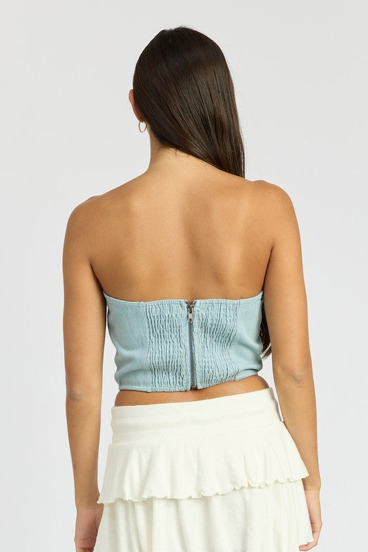 Back view of a woman wearing Emory Park Denim Corset Top With Rosette Detail in light blue denim