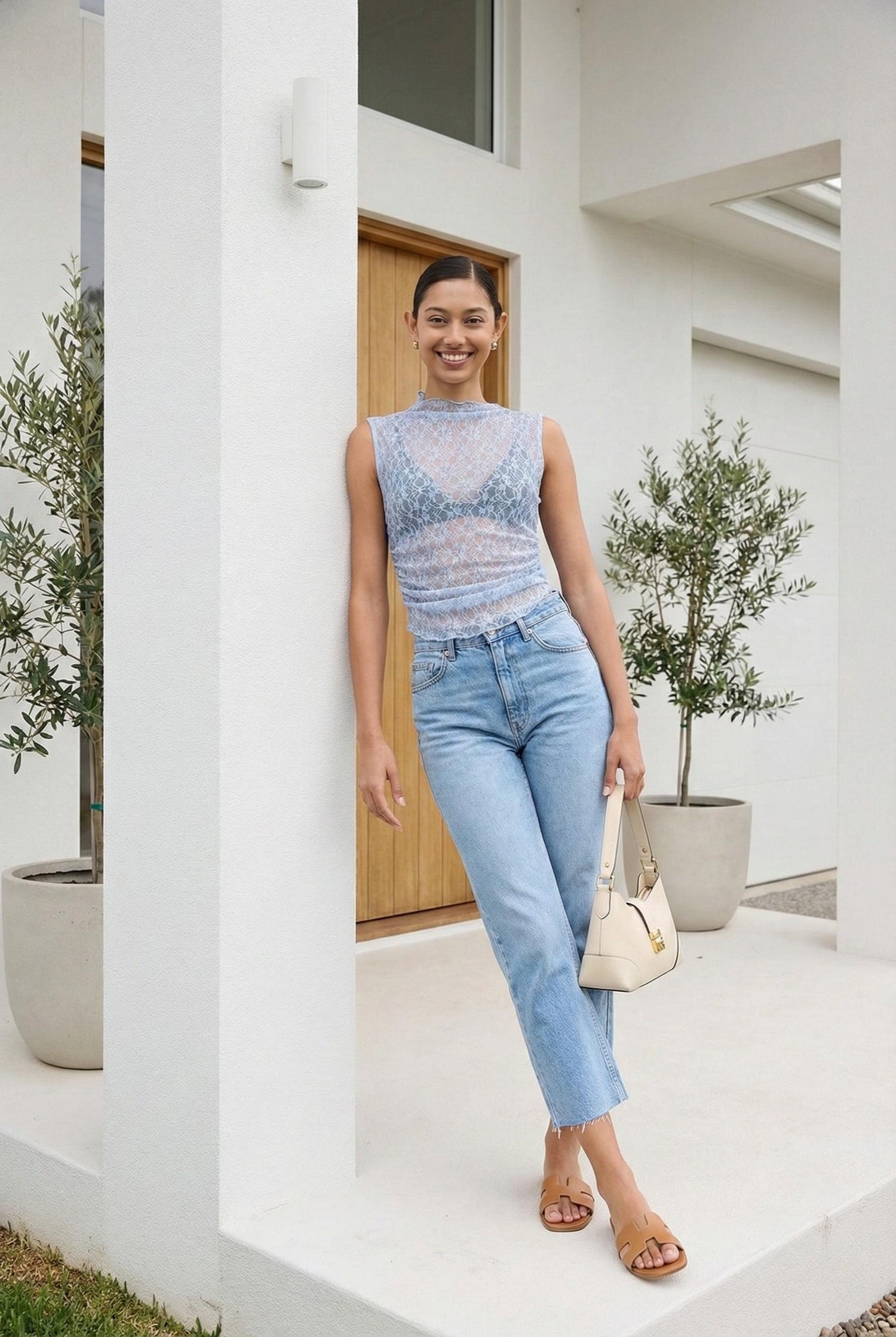 Model wearing Emory Park Lace Mock Neck Sleeveless Top in sheer Dusty Blue lace with jeans and slides posing on luxury porch