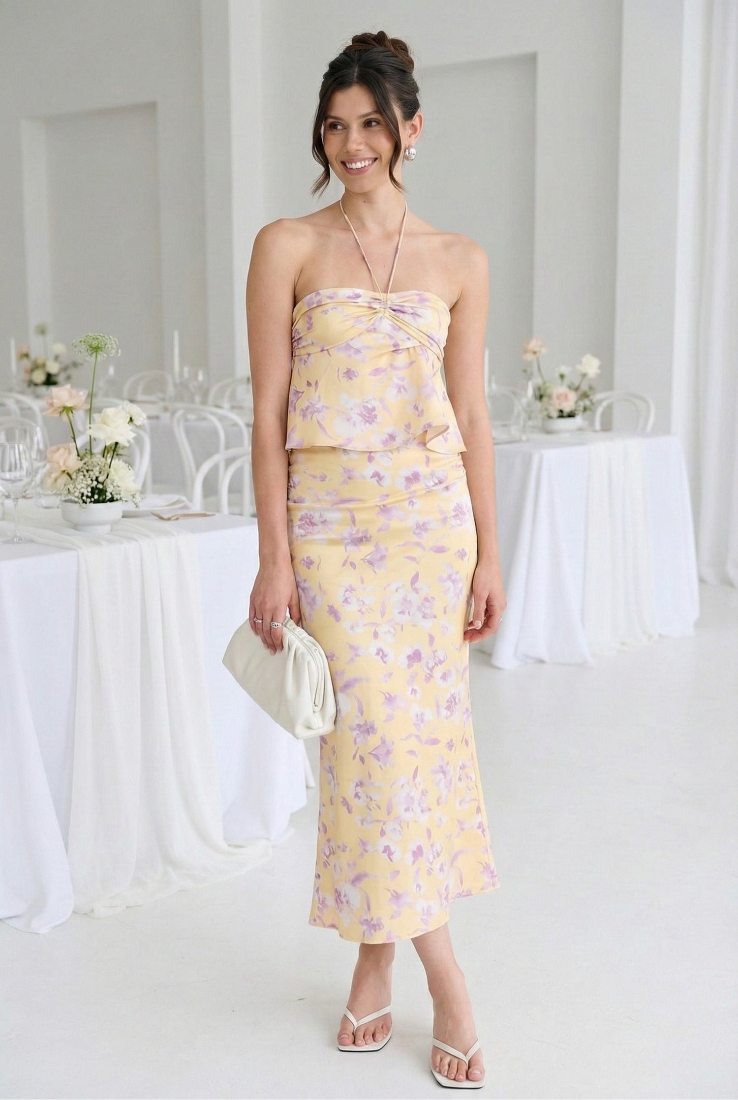 Model wearing Emory Park Floral Strapless Ruched Halter in Yellow with matching floral skirt and sandals standing at wedding reception