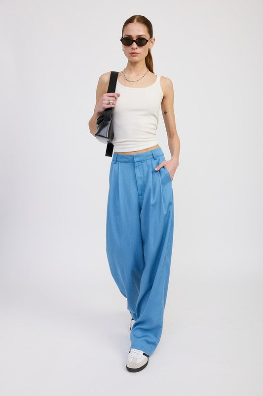 Woman wearing Emory Park high waist wide leg trousers with front pleats in blue styled with white tank top and black sunglasses