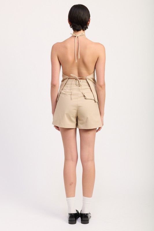 Back view of Emory Park high waisted pleated shorts in beige worn with a halter top and black shoes