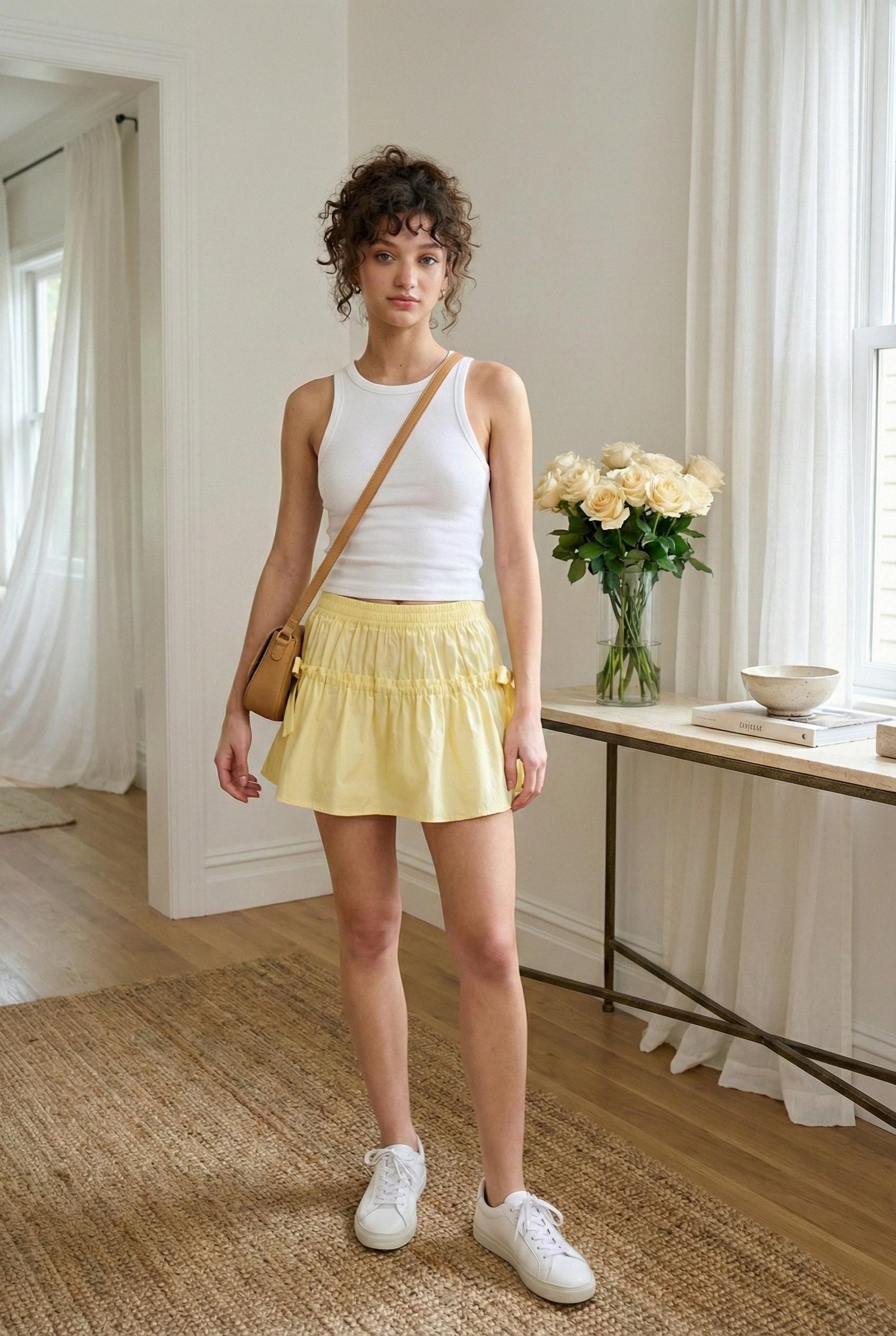 Model wearing Emory Park Mini Ruched Poplin Mini Skirt in soft yellow with side ties paired with tank and sneakers standing in luxury aesthetic home