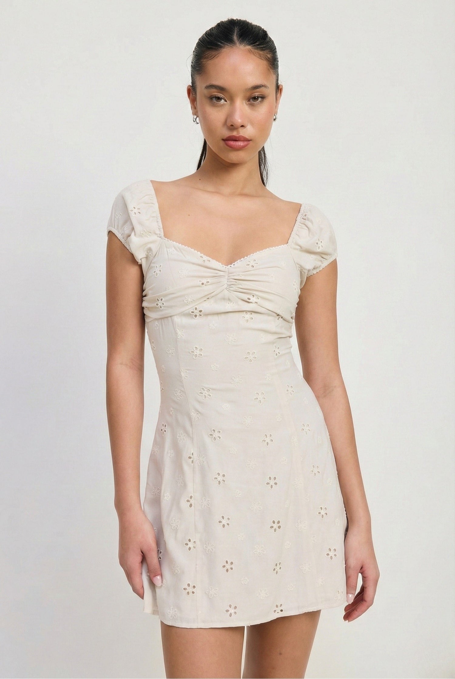 Woman wearing a white dress with floral cut-out details on a plain background