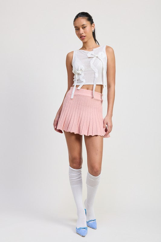 Emory Park pink pleated mini skirt worn with white sleeveless top and knee-high socks knee pose