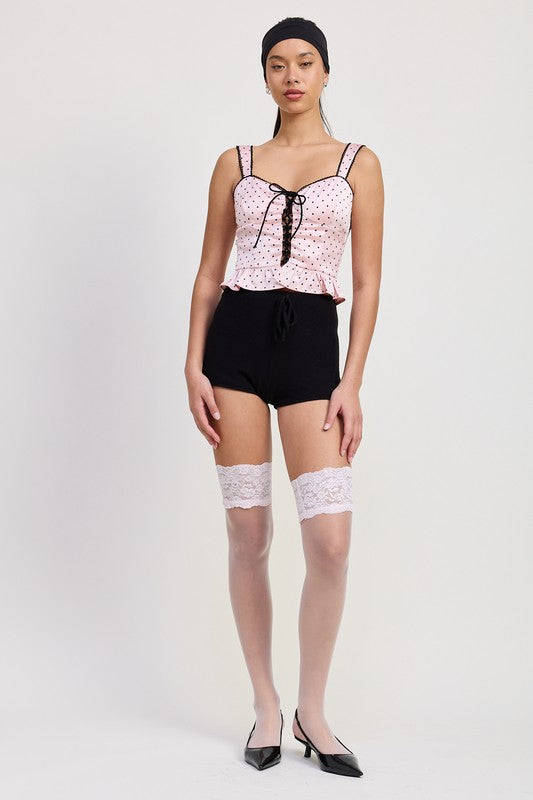 Emory Park Polka Dot Corset Top in pink with black lace-up front worn with black shorts and white lace thigh-high stockings