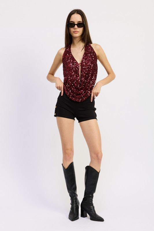 Model wearing a Sequin Cowl Drape Halter Top in burgundy paired with black shorts and boots