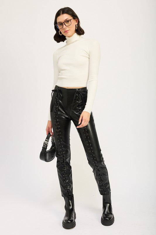Model wearing Emory Park Lace-Up Leather Trousers in black with side lacing and high waist paired with white top and black boots