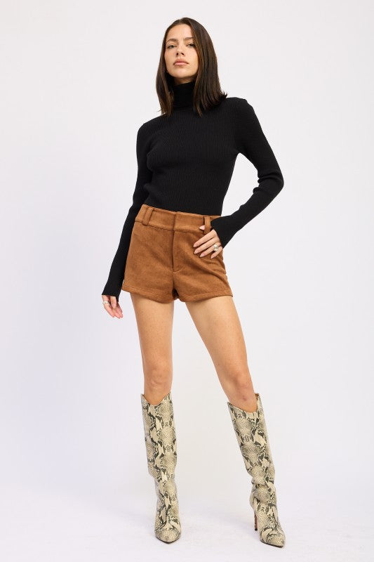 Chic model wearing Suede Low-Rise Shorts with a fitted black top and stylish snake-print boots