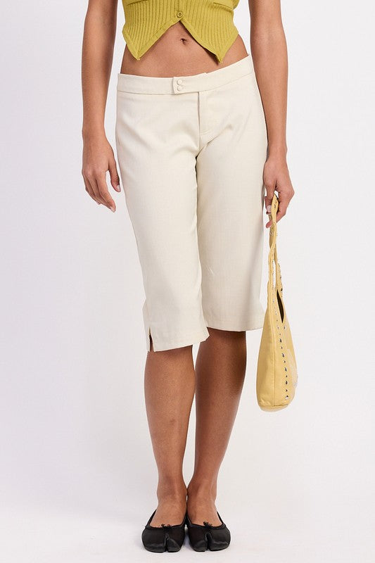 Emory Park model wearing cream Tailored Mid-Rise Bermuda Pants. Knee-length with front slits and yellow handbag