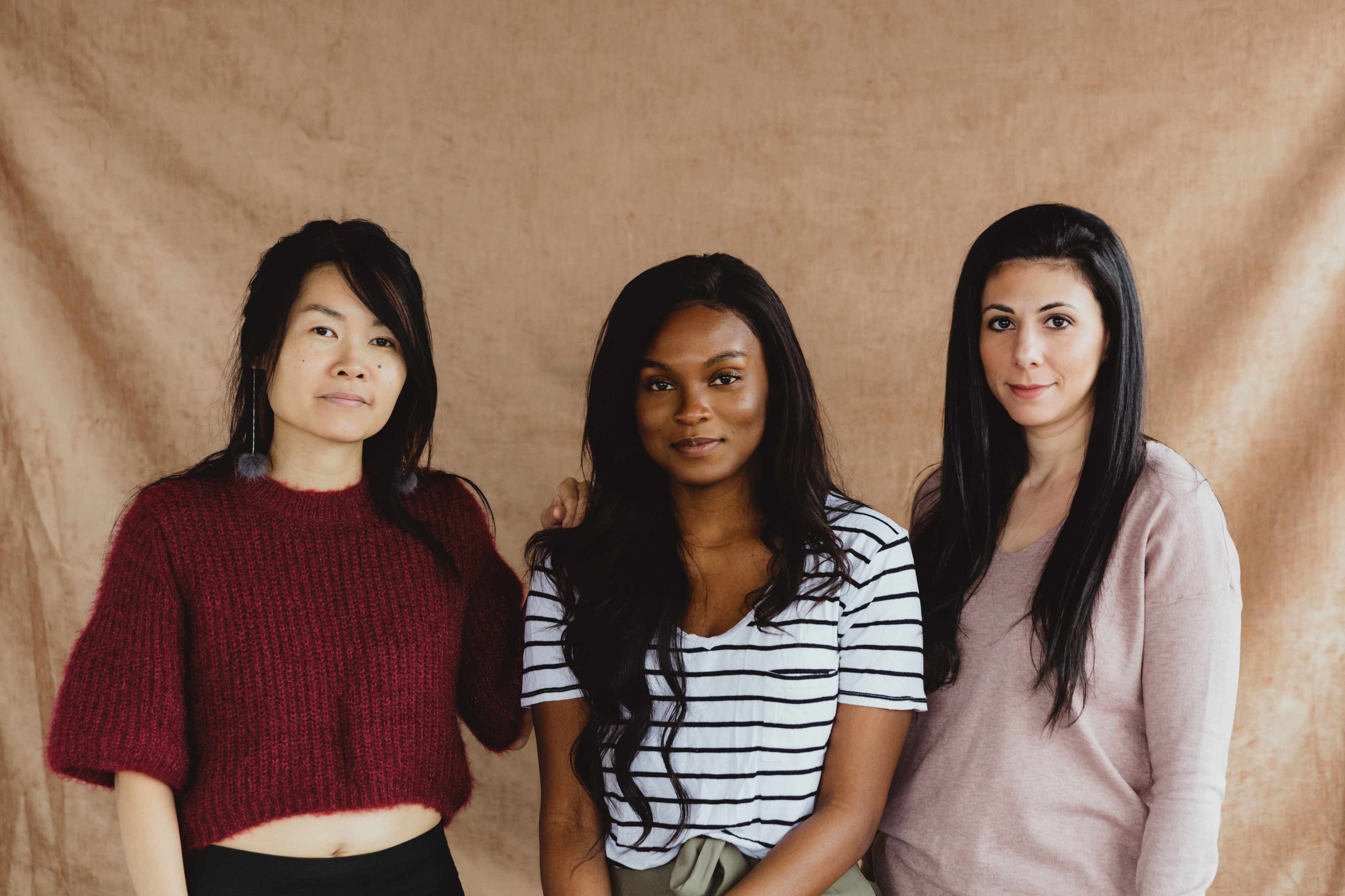 Three women standing side by side against a beige background