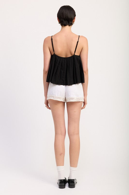 Back view of a woman wearing Emory Park Pleated Tie Front Cami Top in black with adjustable straps and white shorts