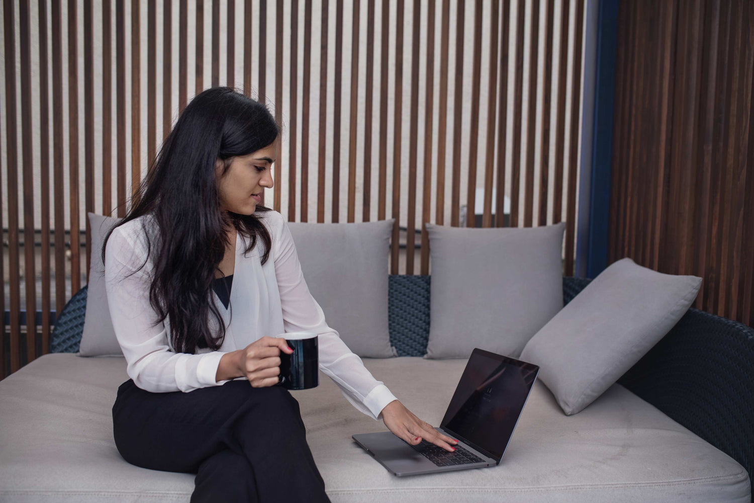 Woman sitting on a couch using a laptop and holding a mug.